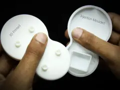 Hands hold two white plastic parts, one labeled "3D Printed" and the other "Injection Moulded," showcasing the difference between the two manufacturing methods.