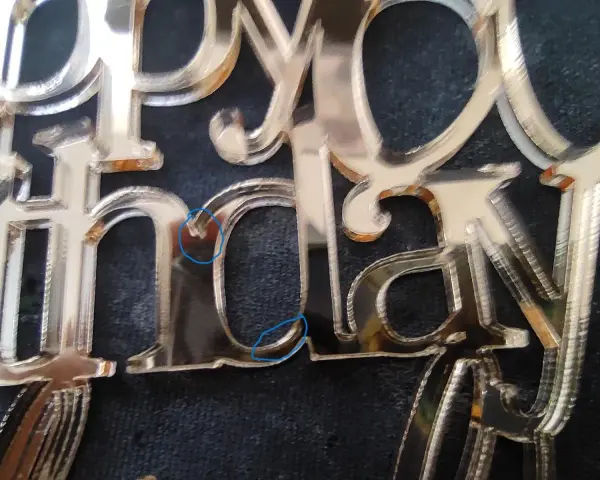 Close-up of a "Happy Birthday" acrylic mirror cake topper, showing the delicate edges and some minor imperfections from how to cut acrylic mirror.