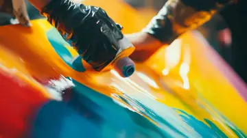 Hands in black gloves apply vibrant acrylic paint to a glossy surface, demonstrating how to paint acrylic plastic with a fluid art technique.