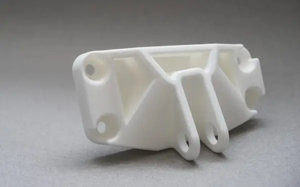 A white, complex SLS part with multiple holes and support structures, ready for assembly.