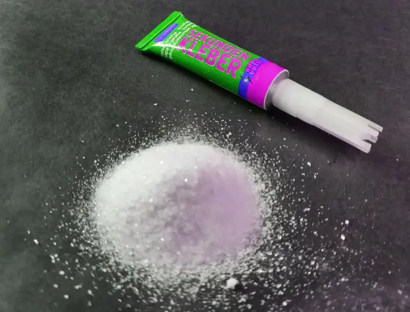 A pile of white granular material sits next to a tube of "Sekunden Kleber" super glue, ready for a quick fix.